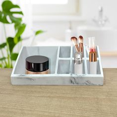 a marble tray with makeup and brushes in it on a wooden table next to a potted plant