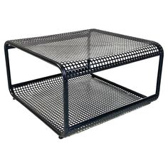 a black metal coffee table with mesh design on the top and bottom shelf, against a white background