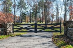 a gated driveway leading to a grassy field and wooded area with trees in the background