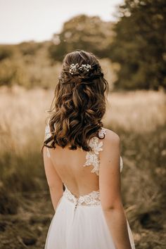 the back of a bride's dress in a field with tall grass and trees