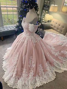 a pink ball gown with white lace on the skirt and off the shoulder, in front of a christmas tree