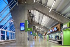 the inside of an airport terminal with green and blue signs hanging from the ceiling in front of large windows