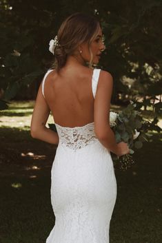 a woman in a white wedding dress holding a bouquet and looking back at the camera