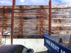 a blue truck parked in front of a wooden wall with rusted metal bars on it's sides