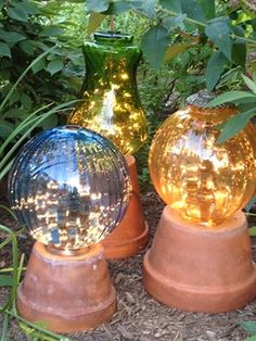 three glass vases sitting on top of terracotta bases in the grass and bushes