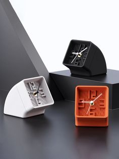 two clocks sitting on top of a black table next to an orange box with a white clock in it