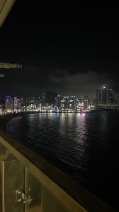 the city lights shine brightly in the dark night sky over the ocean and water, as seen from an observation deck