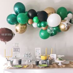 a table topped with balloons and desserts next to a football balloon wall mounted on the wall