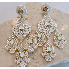 a pair of white and gold earrings sitting on top of a marble slab next to a rock