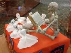 there is a fake skeleton reading a book on the table with ghost figurines