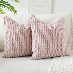 two pink pillows sitting on top of a white couch next to a green leafy plant