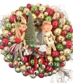 a christmas wreath with ornaments and two small children on the front, hanging from it's side