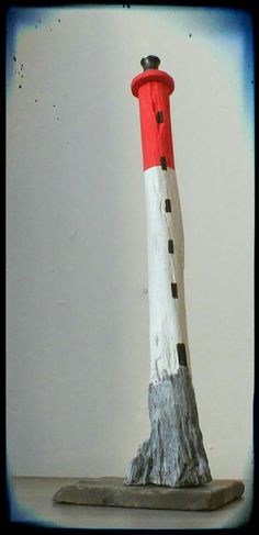 a small red and white lighthouse on top of a wooden block in front of a white wall