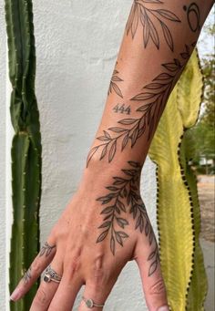 a woman's hand with tattoos on it and a cactus in the back ground