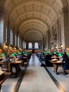 people sitting at tables in a large room with lots of windows and lamps on the ceiling