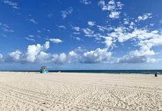 a sandy beach with blue and yellow lifeguard tower in the distance on a sunny day