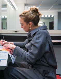 a woman sitting at a desk writing on a piece of paper with a pen in her hand