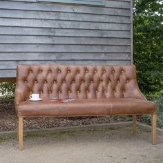 a brown leather couch sitting in front of a wooden bench next to a gray house