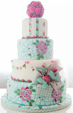 a three tiered cake with pink flowers on it's sides and blue ribbon around the edges