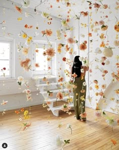 a woman standing in front of a window with flowers falling from the ceiling above her