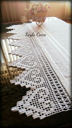 crocheted table runner on top of a wooden table in front of a window