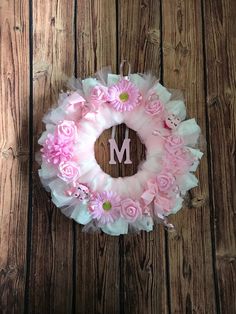 a pink and white wreath with the letter m on it sitting against a wooden wall