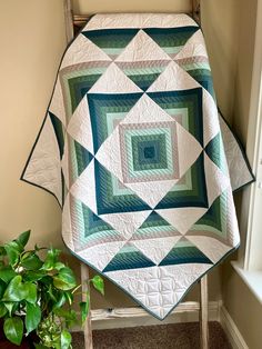 a green and white quilt on a chair next to a potted plant