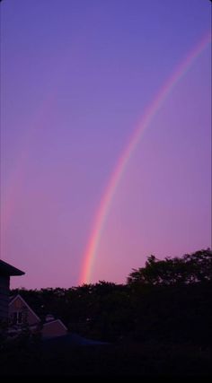 a rainbow is seen in the sky over a house and trees at sunset or dawn