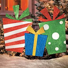 two christmas presents sitting on top of snow next to a tree in front of a house