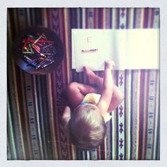 a small child is reading a book on the floor next to a pile of colored pencils