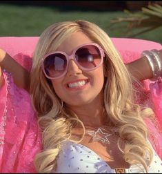 a woman wearing pink sunglasses sitting in a pink chair with her arms behind her head