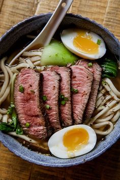 a bowl filled with meat, noodles and an egg on top of a wooden table