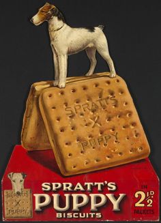 a dog standing on top of a cracker box with the words sprat's puppy biscuits written on it