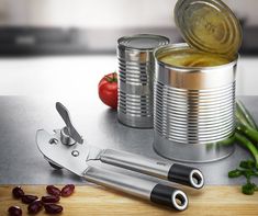 some tins and scissors on a table with tomatoes, beans and olives next to them