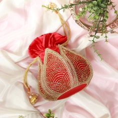 a red and gold purse sitting on top of a pink blanket next to a potted plant