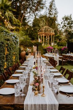 a long table is set with white plates and place settings for an outdoor dinner party