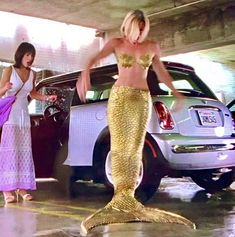 two women in bikinis standing next to a car with a mermaid tail on it