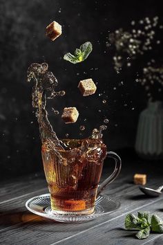 tea being poured into a glass cup with cubes falling off the side and mint leaves in the air