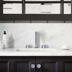 a kitchen with marble counter tops and black cabinets, along with white dishes on the counters