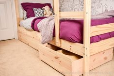 a wooden bunk bed with purple sheets and pillows on it's bottom shelf next to a white door