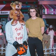 a man standing next to a teddy bear holding a chainsaw