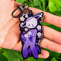 a hand holding a purple and black keychain with a cartoon character on it