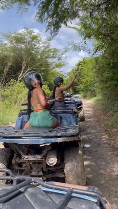 two people riding on the back of an atv down a dirt road with trees in the background