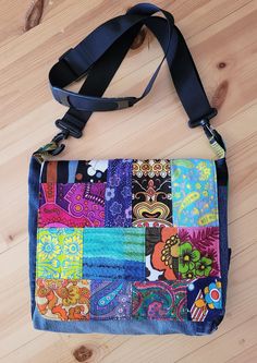 a multicolored patchwork purse sitting on top of a wooden floor next to a black strap