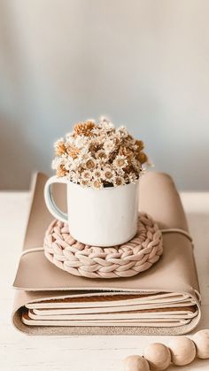 a white coffee cup filled with flowers on top of a stack of coasters and wooden beads