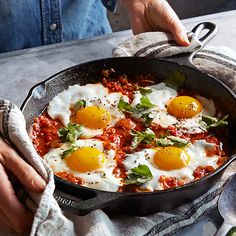 two fried eggs are in a skillet with tomato sauce and herbs on the side