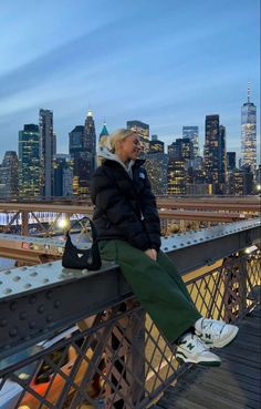 a woman sitting on top of a metal fence next to a tall cityscape