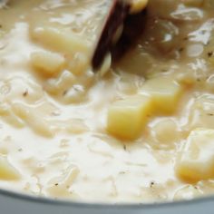 a pot filled with soup and potatoes being stirred by a ladle to stir it