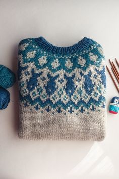 a blue and white sweater sitting on top of a table next to knitting needles