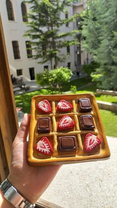 a person holding a plate with chocolates on it in front of a building and trees